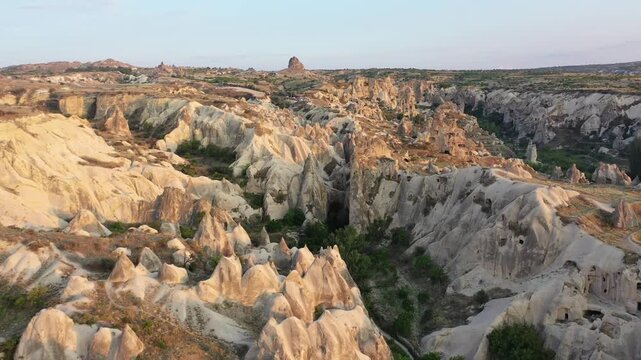 Panoramic aerial drone view of iconic fairy chimney rock formations and steep eroded tuff mountain ridges in Love Valley, Cappadocia, Nevsehir, Turkey during golden hour.