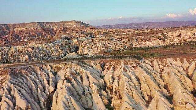 High aerial drone view of vast deeply eroded tuff rock ridges and canyons bathed in warm golden hour light in Red Valley, Cappadocia, Nevsehir, Turkey on a sunny day.