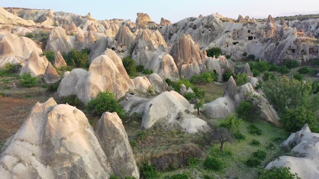 Panoramic aerial drone view of iconic fairy chimney rock formations and steep eroded tuff mountain ridges in Love Valley, Cappadocia, Nevsehir, Turkey during golden hour.