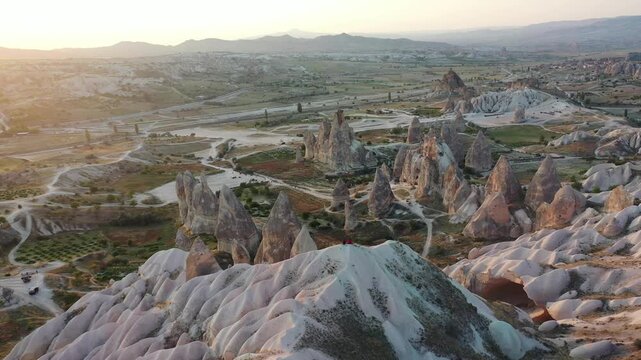 Panoramic aerial drone view of iconic fairy chimney rock formations and steep eroded tuff mountain ridges in Love Valley, Cappadocia, Nevsehir, Turkey during golden hour.