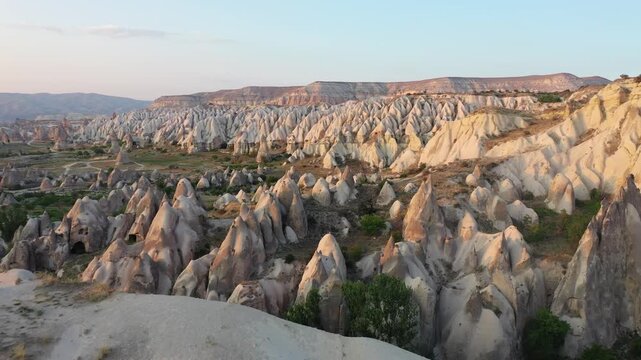 High aerial drone view of ancient rock-cut cave dwellings and historical cave houses carved into volcanic tuff in Goreme, Cappadocia, Nevsehir, Turkey at golden hour.