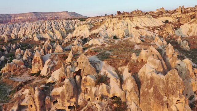 High aerial drone view of ancient rock-cut cave dwellings and historical cave houses carved into volcanic tuff in Goreme, Cappadocia, Nevsehir, Turkey at golden hour.