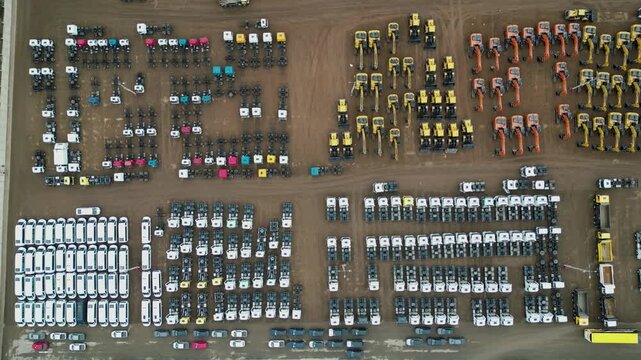 Cinematic drone footage of a heavy equipment storage facility featuring geometric rows of excavators, buses, and commercial trucks parked outdoors.