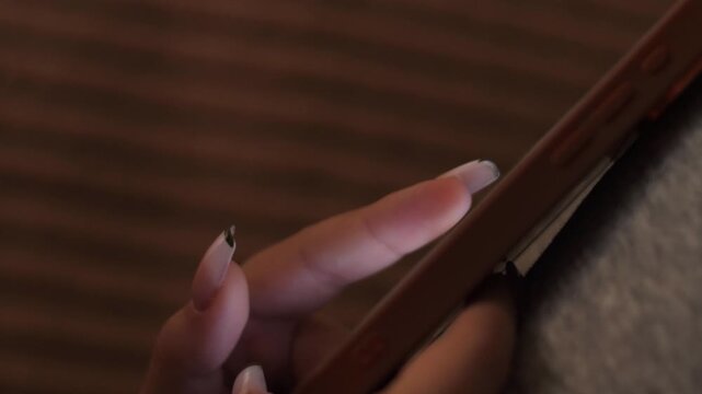 A woman's finger with a neat French manicure smoothly scrolls through the feed on a smartphone screen. Close-up shot of using a mobile phone for social media or reading news in the evening