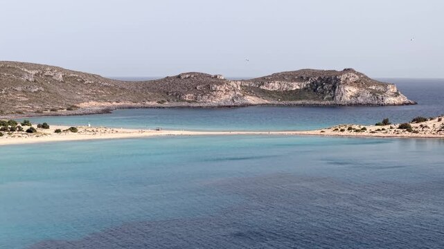Simos beach double bay with rugged limestone mountain in background into Aegean Sea, Elafonisos island, Drone view