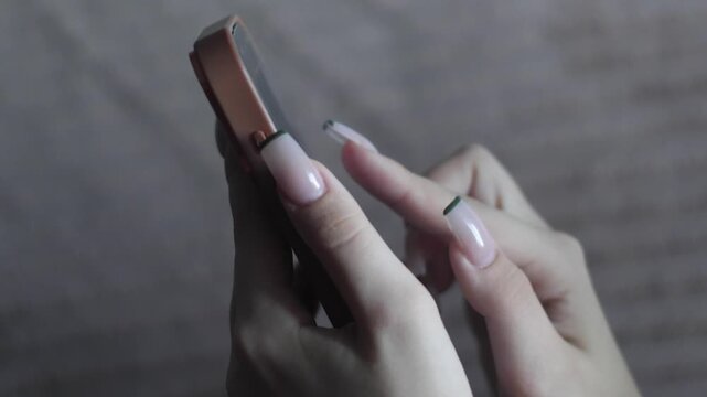 Female hands with a beautiful French manicure hold a smartphone and actively tap on the screen. Close-up shot of using a mobile phone for messaging and browsing content on the Internet