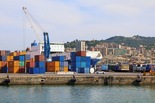 Genoa, Italy - 29 August 2018: View of Genova Harbor industrial area with stacked colorful shipping containers, a large cargo ship, and a crane against the backdrop of the city skyline.