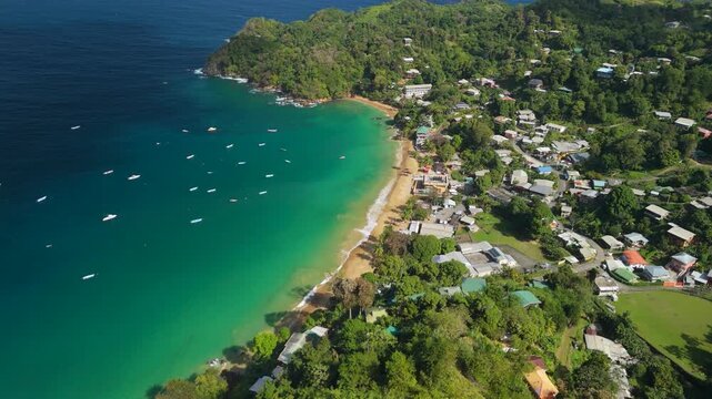 Aerial view shows Castara Bay turquoise waters dotted with fishing boats sandy beach and hillside village Tobago Caribbean