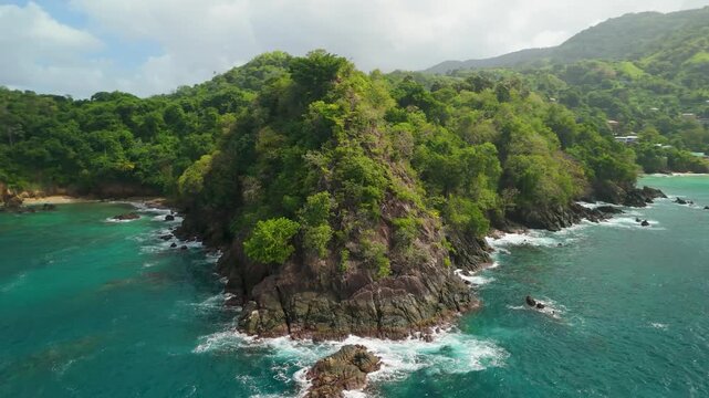 Drone reveals rugged forested headland and rocky coastline giving way to turquoise waters of Castara Bay Tobago Caribbean