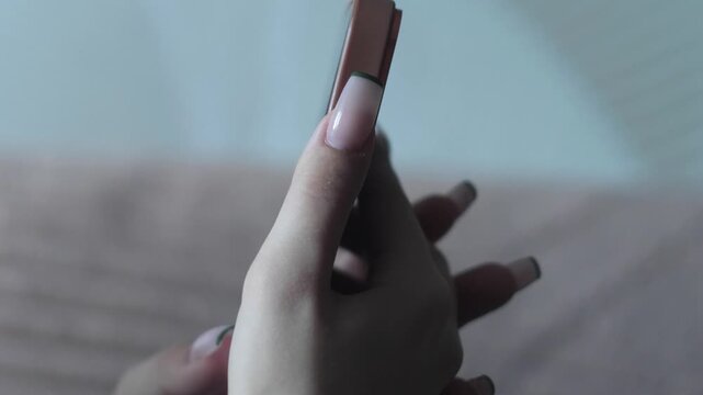 Female hands with an elegant French manicure carefully hold a modern smartphone. Close-up shot of using a mobile phone for work, messaging, and content browsing