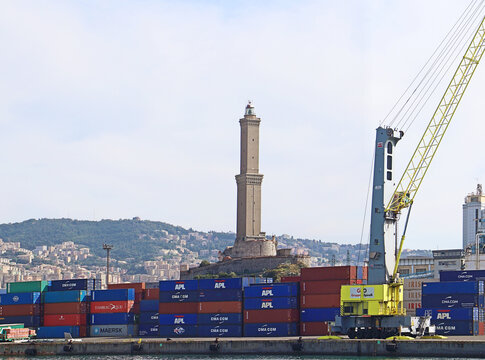 Genoa, Italy - 29 August 2018: View of the historic Lanterna lighthouse rising above colorful shipping containers and a large industrial crane at the port of Genoa, Liguria, Italy.