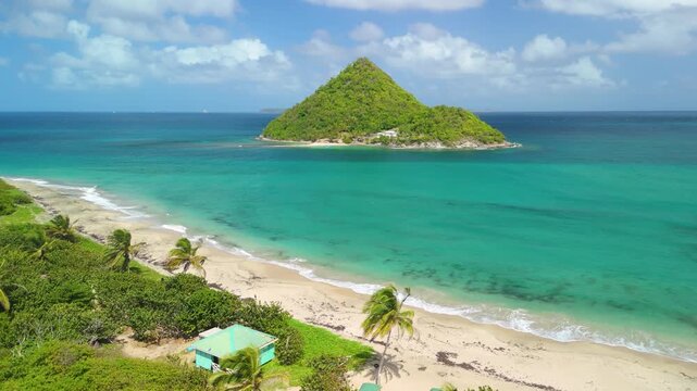 Aerial parallax shot glides over palm lined Levera Beach in Grenada revealing turquoise water and pyramid shaped Sugar Loaf Island