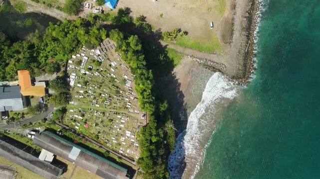 Aerial top down descent reveals Leapers Hill Cemetery in Sauteurs Grenada perched above beach and turquoise Caribbean sea