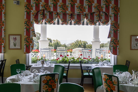 Mackinac Island, Michigan, United States - 15 August 2025: View of the dining room at Mackinac Island with floral curtains, white porch chairs, and garden views.