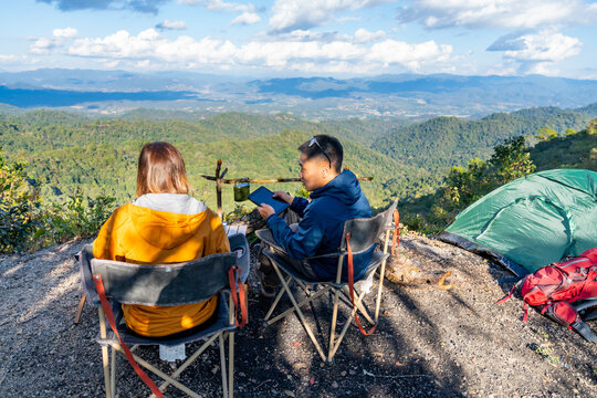 Asian man and woman remote working corporate business on digital tablet and smartphone while travel nature camping in forest with drinking coffee. Digital nomad workation outdoor active lifestyle
