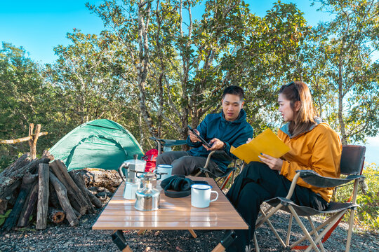 Asian man and woman remote working corporate business on digital tablet and smartphone while travel nature camping in forest with drinking coffee. Digital nomad workation outdoor active lifestyle