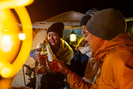 Group of Adult friends camping on mountain, drinking beer with toasting beer bottle together by tent. Man and woman enjoy outdoor active lifestyle friendship travel forest nature on holiday vacation.