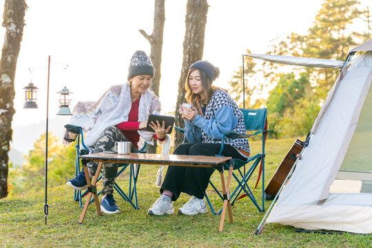 Asian woman colleague remote working corporate business meeting discussion with using digital tablet while camping on the mountain with drinking coffee. Digital nomad workation outdoor lifestyle
