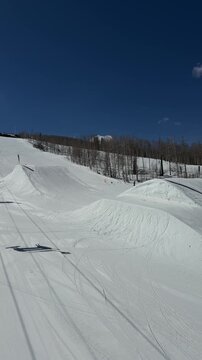 Tracking shot of terrain park jumps on snowy mountain from moving chairlift at ski resort