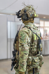 Fototapeta premium Mannequin in camouflage uniform, side profile view, tactical vest with pouches, helmet with communication device, blurred industrial background, even diffused lighting, muted earthy tones, military