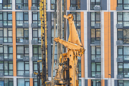 Drilling rig engaged in construction task, vibrant colors contrast against urban building facade, modern architectural style with orange and gray panels, soft natural daylight enhancing details