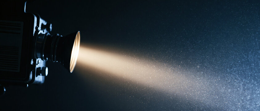 A vintage film camera shines a bright beam of light through the dark air filled with floating dust particles to create a cinematic atmosphere for a movie production