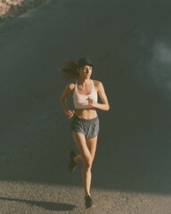 Obraz premium Young Woman Jogging Outdoors on a Paved Road During Daylight, Focused and Fit
