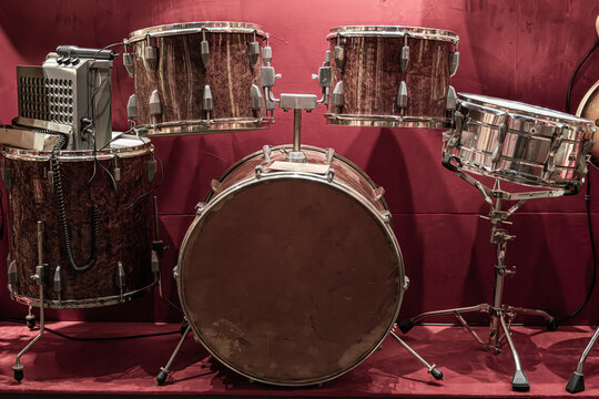 Drum set arranged against vibrant red backdrop, featuring dark marbled finish drums, metallic hardware, clean studio lighting, balanced composition