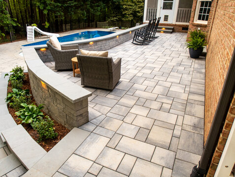 Elevated Wide View Of Modern Stone Paver Patio With Retaining Walls Seating And Inground Swimming Pool