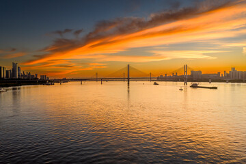 Naklejka premium Stunning sunrise over the Yangtze River in Wuhan, China. A majestic cable-stayed bridge spans the golden water beneath vibrant fiery clouds, showcasing impressive modern engineering and architecture.