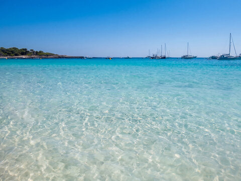 Eau turquoise cristalline avec voiliers ancr&eacute;s au loin sous un ciel bleu pur, paysage marin m&eacute;diterran&eacute;en id&eacute;al pour la baignade et la navigation