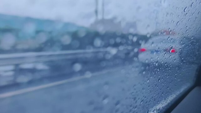 Rain droplets covering car window overlooking blurred highway traffic on rainy day