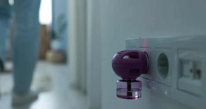 Man plugging in electric mosquito repeller with liquid refill and walking away at home, closeup
