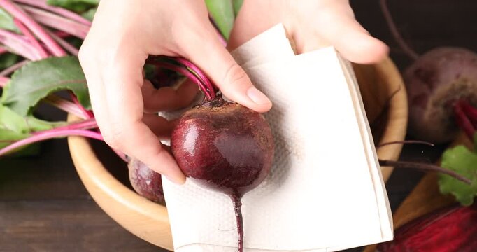 Woman wiping fresh young beet with paper towel at table, closeup