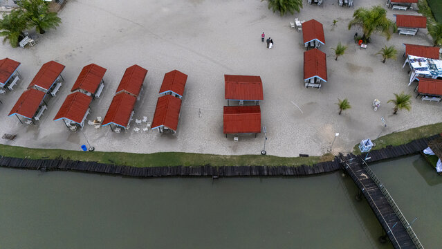 Aerial view of McCarthy beach featuring rows of red-roofed cabanas on sandy ground, a wooden pier extending into the water, and palm trees in Urhuoka, Delta, Nigeria.