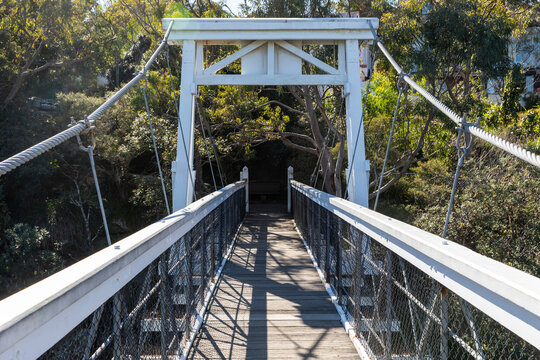 Old Wood Suspension Walking Bridge over water in bush setting on sunny day with blue sky. Walkway and landscape. Wide view along walkway