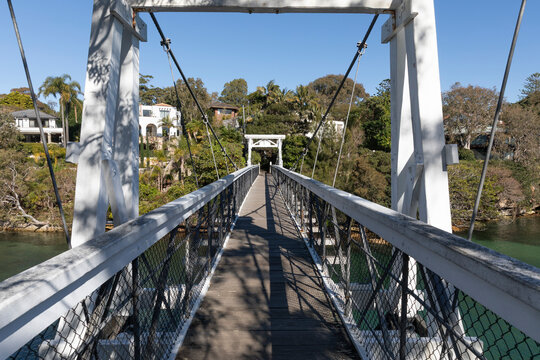 Old Wood Suspension Walking Bridge over water in bush setting on sunny day with blue sky. View along walkwway