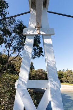 Old Wood Suspension Walking Bridge over water in bush setting on sunny day with blue sky. Wooden structure detail
