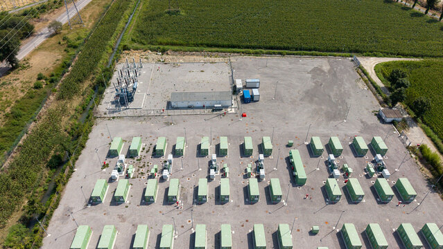 Aerial view of the BESS battery storage facility with rows of green containers and an electrical substation surrounded by agricultural fields in Tavazzano con Villavesco, Lombardy, Italy.
