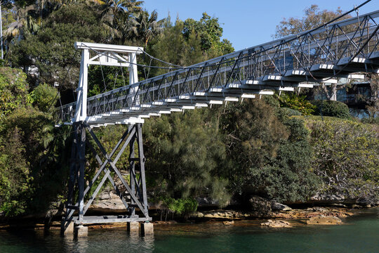 Old Wood Suspension Walking Bridge over water in bush setting on sunny day with blue sky. Pylon and walkway.