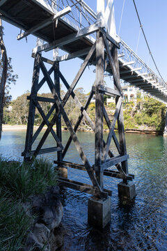 Old Wood Suspension Walking Bridge over water in bush setting on sunny day with blue sky. Pylon view.