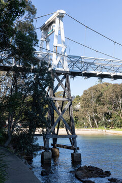 Old Wood Suspension Walking Bridge over water in bush setting on sunny day with blue sky. View of pylon
