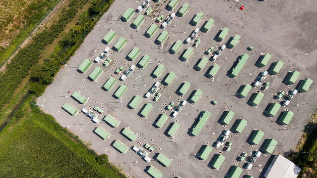 Aerial view of BESS Battery Storage Facility with rows of green energy storage containers on a gravel lot in Tavazzano con Villavesco, Lombardy, Italy.