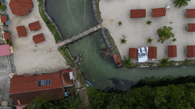 Aerial view of McCarthy beach featuring a wooden bridge over turquoise water, surrounded by sandy shores, red-roofed huts, and palm trees in Urhuoka, Delta, Nigeria.