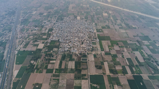 Aerial view of a rural town surrounded by a vast patchwork of agricultural fields and irrigation canals in Punjab, Pakistan.