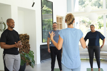 Naklejka premium Diverse friends following female coach leading fitness session in living room on mats in sportswear