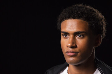 Obraz premium African American man posing in studio, dark jacket and white T-shirt highlighting face, copy space