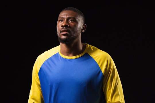 African man posing in studio wearing blue and yellow athletic shirt, gazing slightly upward