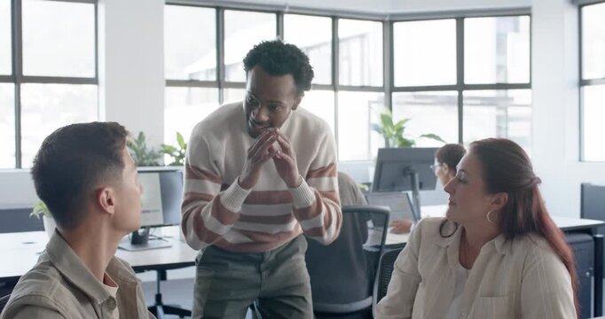 Diverse coworkers listening, standing man approaching desk, gesturing, explaining plan with laptop