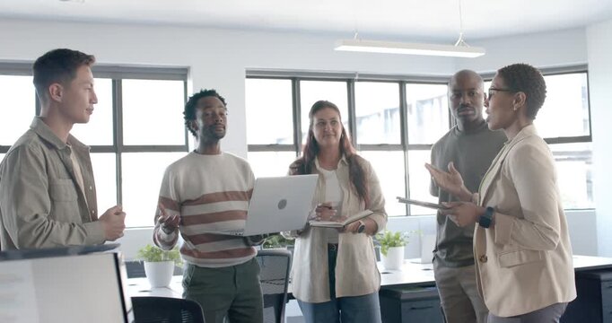 Diverse coworkers presenting laptop for input after tan blazer speaker tapping tablet in office